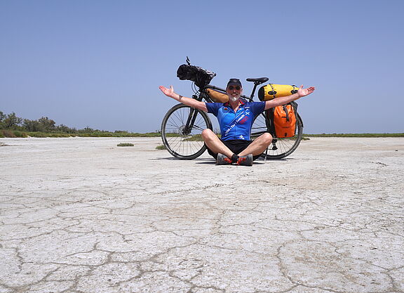 Thomas Meier am Strand im Schneidersitz vor seinem bepacktem Fahrrad sitzend