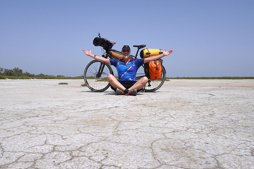 Thomas Meier am Strand im Schneidersitz vor seinem bepacktem Fahrrad sitzend