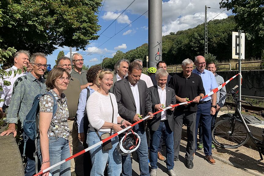 Bürgermeister und andere Leute stehen auf dem zu eröffnenden Rheinradweg und schneiden mit der Schere ein Band durch