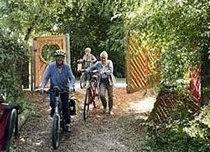 Drei sich auf einem Waldweg befindende Fahradfahrende . hinter ihnen ein offenes Holztor