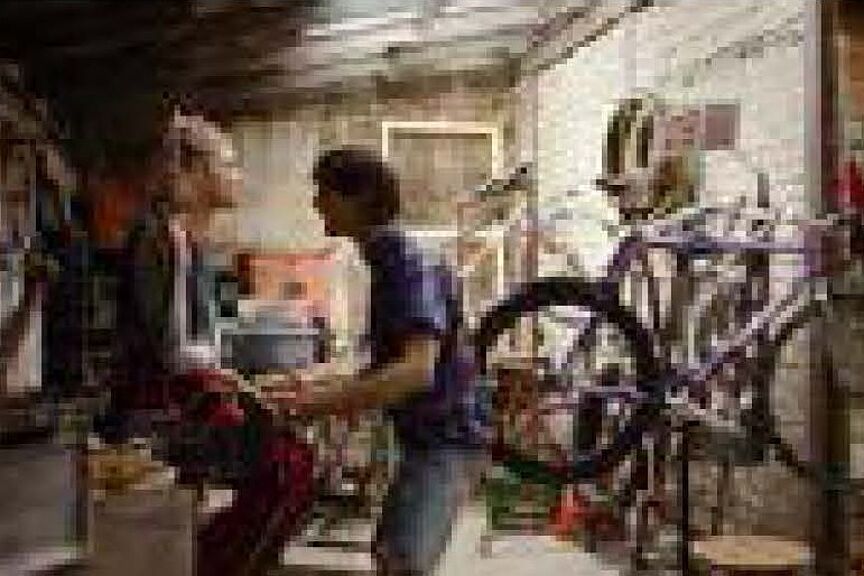 Filmszene: In einer Fahrradwerkstatt sitzt eine Frau auf einem rbeitstisch und ein Mann steht auf sie einredend vor ihr