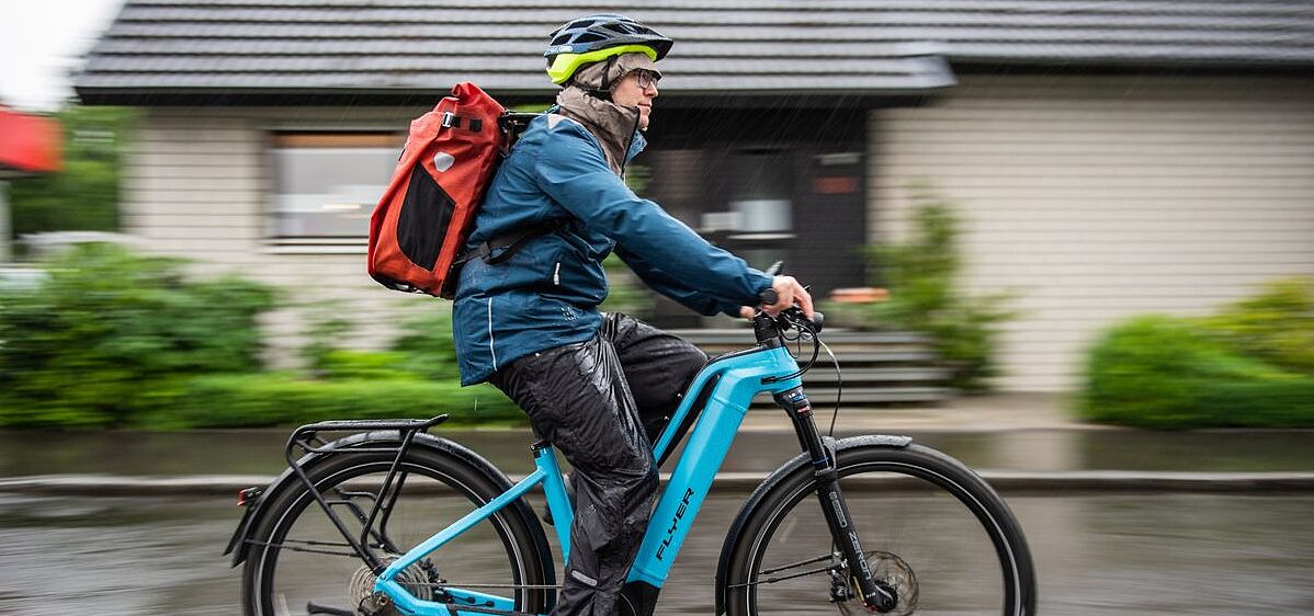 Nässe Radfahrer von der Seite aufgenommen auf Pedelec im Regen unterwegs.